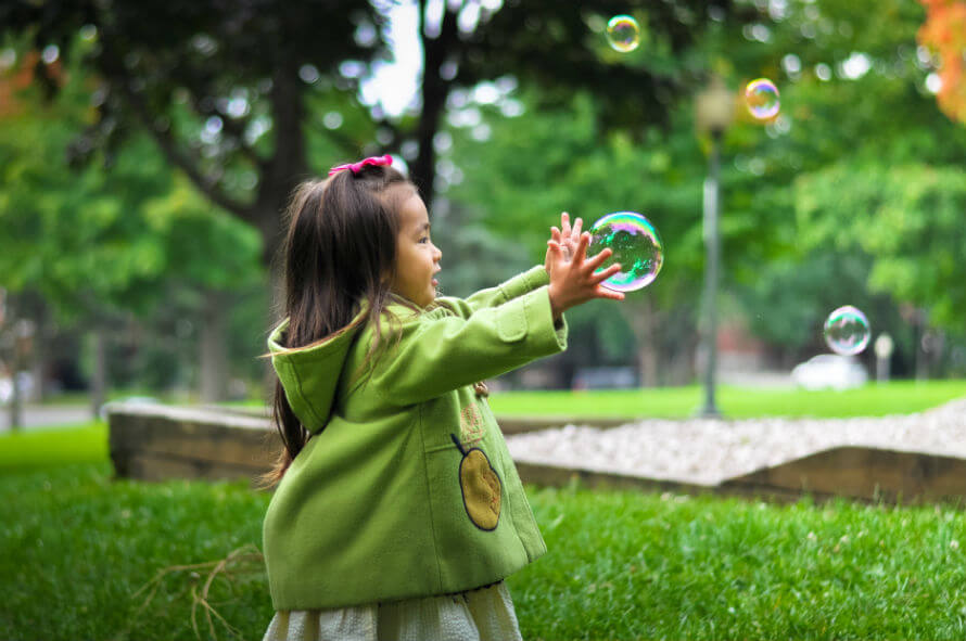 A young girl outside chasing bubbles