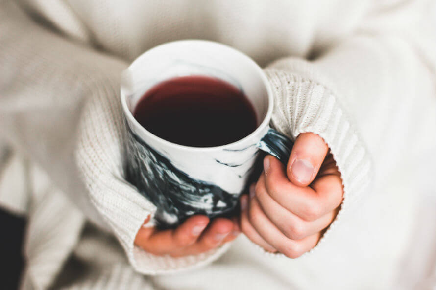 Hands of woman in jumper holding mug of tea