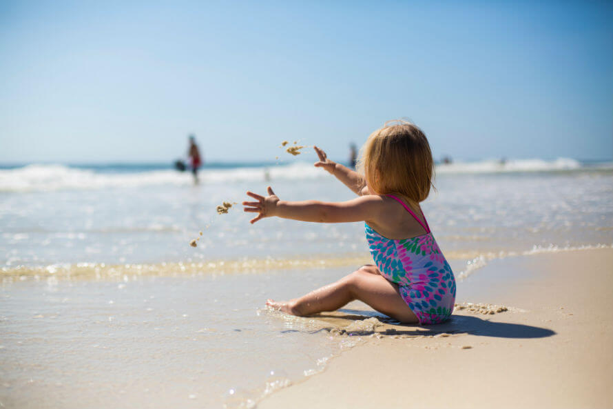 Girl toddler sitting on beach throwing sand