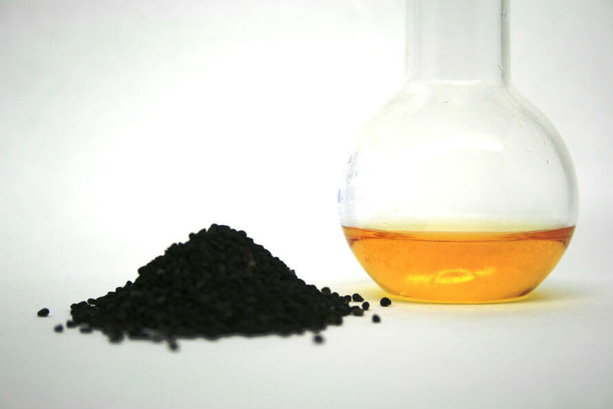 A pile of black seeds next to a glass bottle of black seed oil