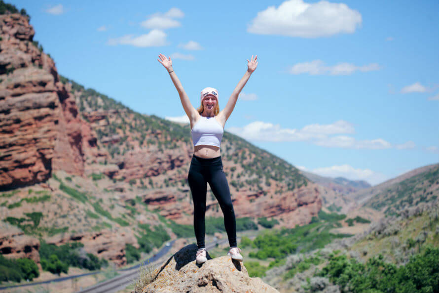 Woman standing on top of rock with both arms raised