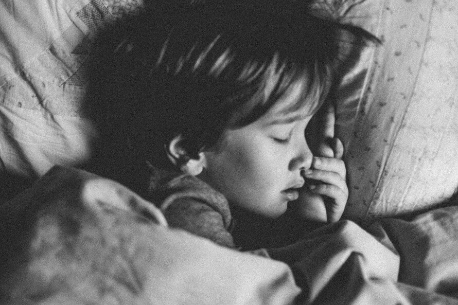 Black and white image of boy sleeping in bed 