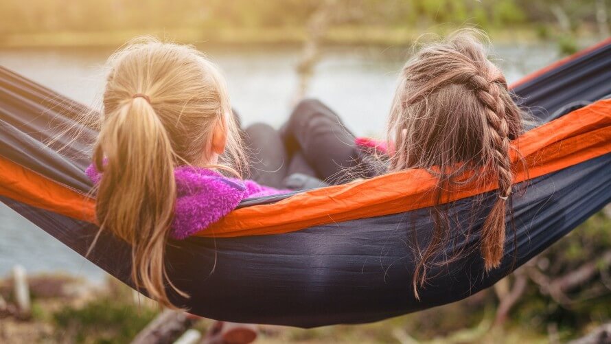 The backs of the heads of two girls with long hair lying on a hammock outdoors