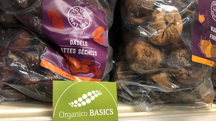 Package of dried dates next to dried figs on shelf. Green Organico BASICS label in front sticking to shelf. 