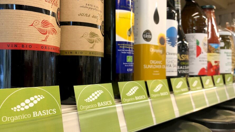 Shelf filled with grocery products. Green Organico BASICS labels sticking to the front of the shelf. 