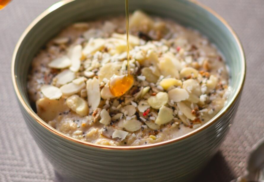 Bowl of porridge topped with nuts, chia seeds, and honey drizzled over.