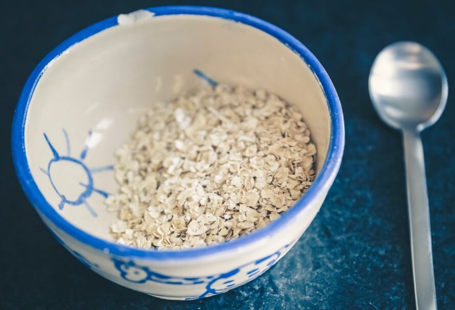Green and white bowl of raw oats next to a spoon. 