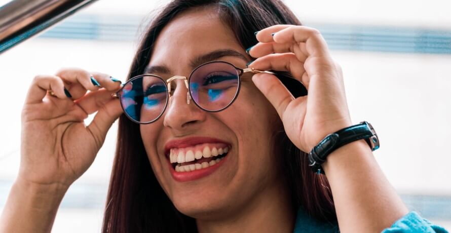 Young woman smiling as she puts on her glasses. 