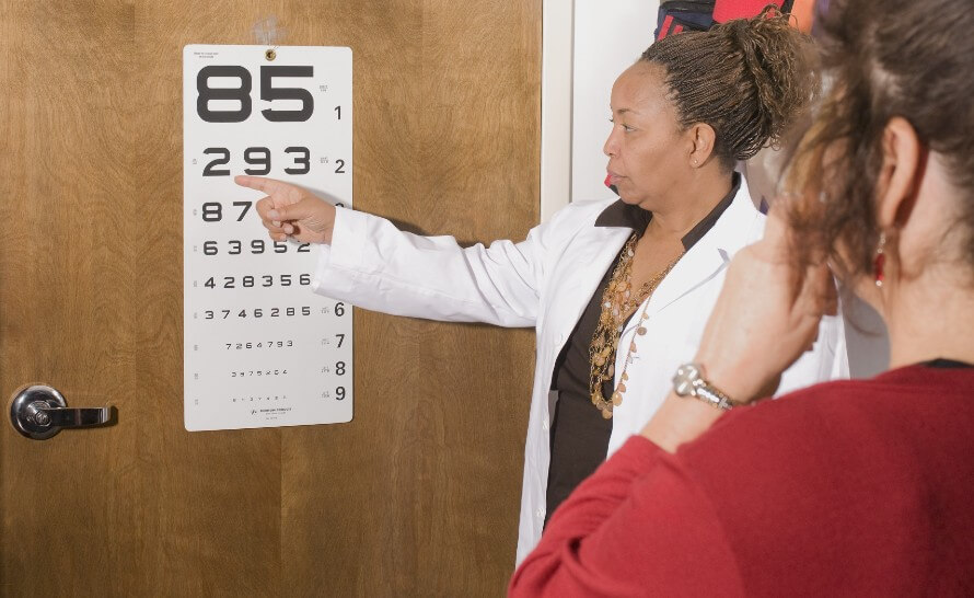 Woman with a doctor having an eye exam. Reading numbers off a poster affixed to the office door.