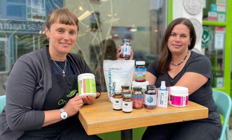 Rachel and Hannah sitting at table outside Organico shop with a selection of magnesium supplements. 