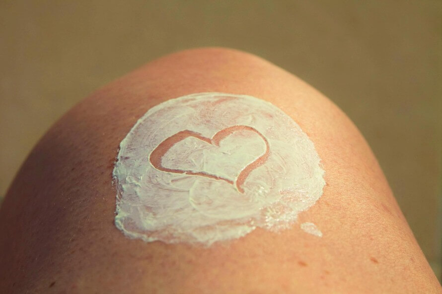 Closeup of someone's knee with a thick circle of sunscreen and a heart drawn by finger in the middle. 