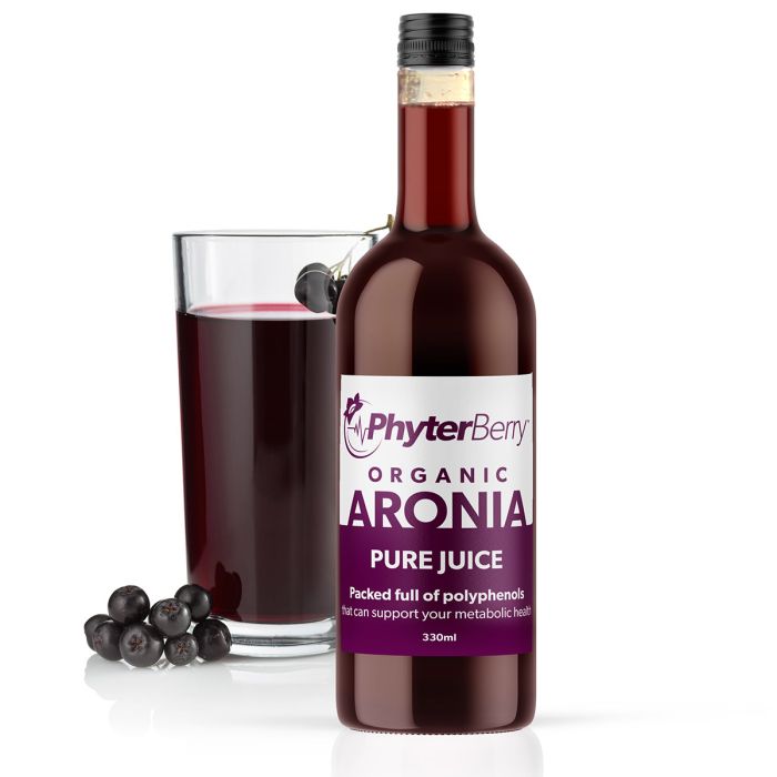 Bottle of aronia juice in front of a glass filled with juice and two clusters of aronia berries. 