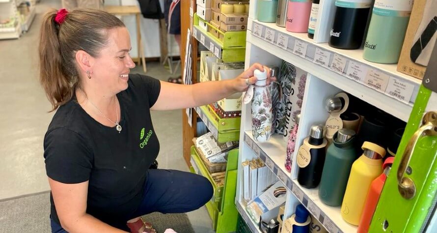 Hannah smiling as she places a water bottle on a shelf inside Organico. 